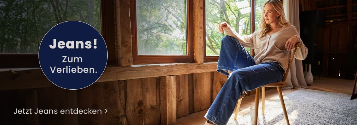 Jeans! Zum Verlieben – Frau in weiter Jeans sitzt entspannt auf Stuhl vor großen Fenstern in Holzraum