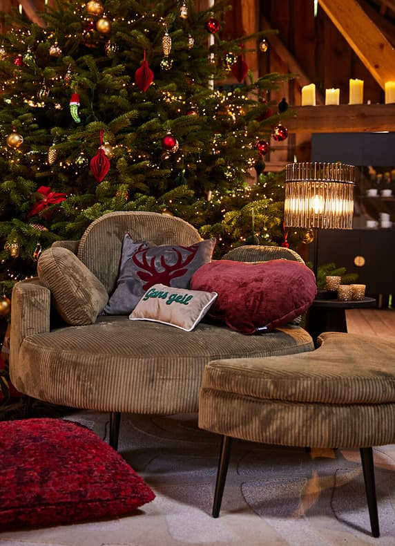 Gans geil Kissen auf rundem Sessel mit Herz- und Rentierkissen vor geschmücktem Weihnachtsbaum und leuchtender Stehlampe