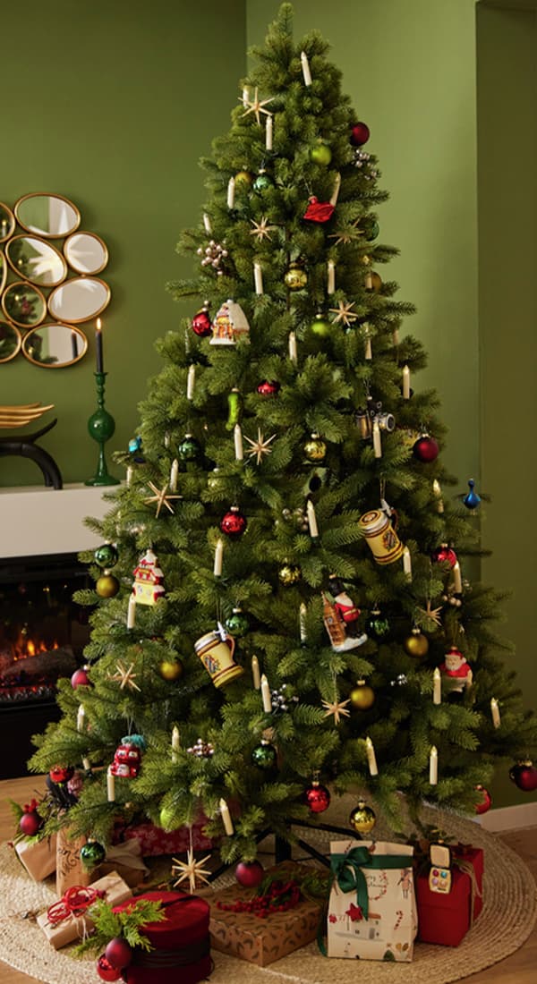 Weihnachtsbaum mit roten und grünen Kugeln, Kerzen und Spielzeug dekoriert. Geschenke liegen unter dem Baum neben Kamin und Spiegel.