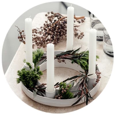 Schlichter Adventskranz mit vier weißen Kerzen, dekoriert mit grünen Zweigen und braunen Beeren auf einem Tisch