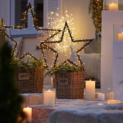 Weihnachtliche Dekoration – zwei Körbe mit Sternen aus Lichterketten, Kerzen auf Treppe, Fenster im Hintergrund