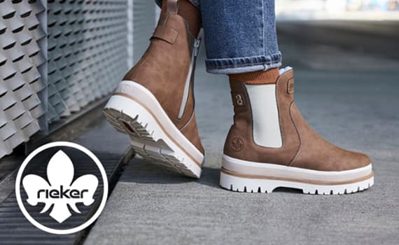 rieker – Person trägt braune Stiefeletten mit weißer Sohle und Reißverschluss, Jeans hochgekrempelt, steht auf Gehweg