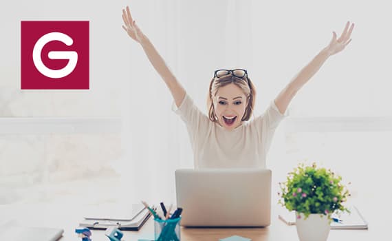 Person am Schreibtisch mit Laptop, jubelt mit erhobenen Armen. Büroartikel und Pflanze im Vordergrund. Logo links.