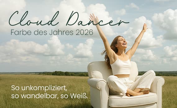 Cloud Dancer Farbe des Jahres 2026 – Frau in weißem Outfit sitzt mit erhobenen Armen im Sessel auf grünem Feld vor bewölktem Himmel