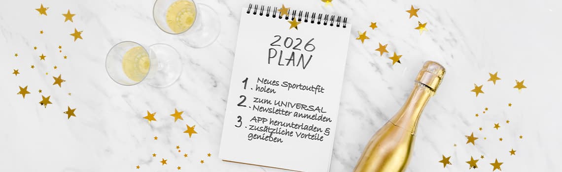 2026 Plan - Notizblock mit Neujahrsvorsätzen, zwei gefüllte Sektgläser, goldene Sterne, goldene Sektflasche auf Marmortisch