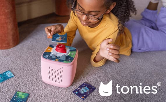 Kind spielt mit Tonies Box und Karten auf Teppichboden