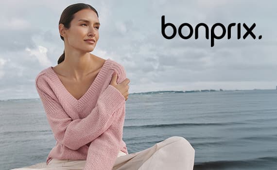 Bonprix – Frau in rosa Pullover sitzt entspannt vor Meer und Wolkenhimmel