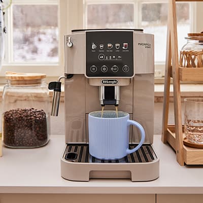 Kaffeemaschine bereitet Kaffee in hellblauer Tasse zu, umgeben von Gläsern mit Kaffeebohnen und Keksen in gemütlicher Küche.