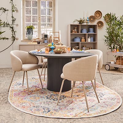 Esszimmer mit rundem Tisch, vier Stühlen und farbigem Teppich, dekoriert mit Geschirr und Pflanzen