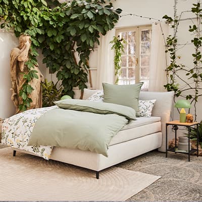 Gemütliches Schlafzimmer mit grünem Bettzeug, Pflanzen und einer Statue, die eine entspannte Atmosphäre schafft.