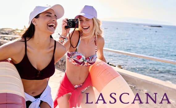 LASCANA – Zwei Frauen in Bademode am Strand, eine macht ein Foto, beide tragen Hüte.