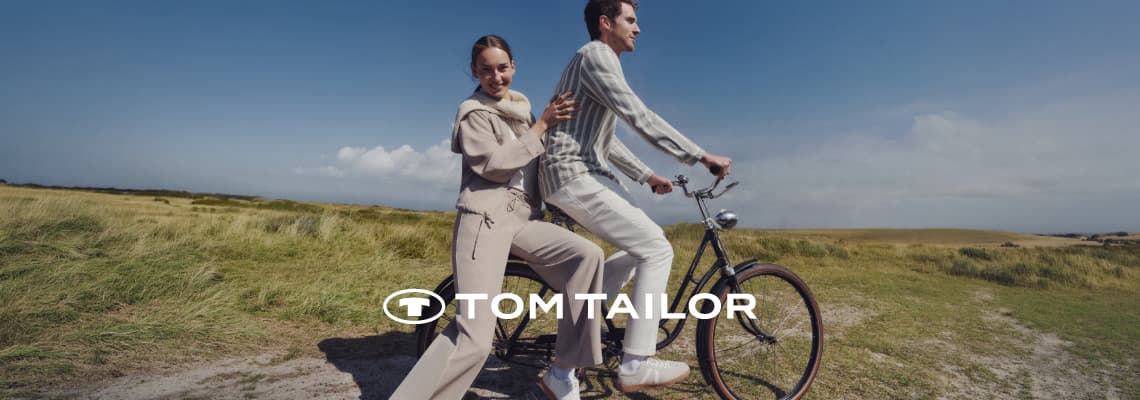 TOM TAILOR – Paar in heller Kleidung fährt auf einem Fahrrad durch eine weite Landschaft