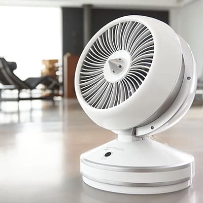 Weißer Tischventilator mit rundem Schutzgitter steht in modernem, hellen Wohnraum auf dem Boden