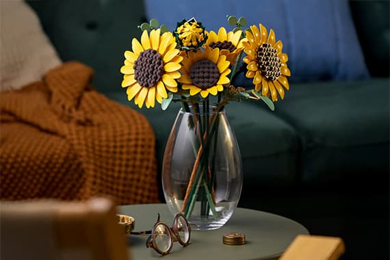 Strauß aus fünf Sonnenblumen in klarer Vase auf Couchtisch, dahinter Sofa mit Decke und Kissen